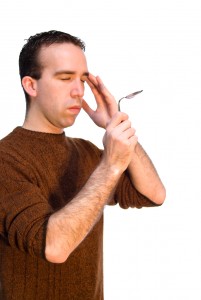 Young man bending a metal spoon with the power of his mind, isolated against a white background